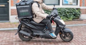 Homem a conduzir moto de entrega de comida Uber Eats